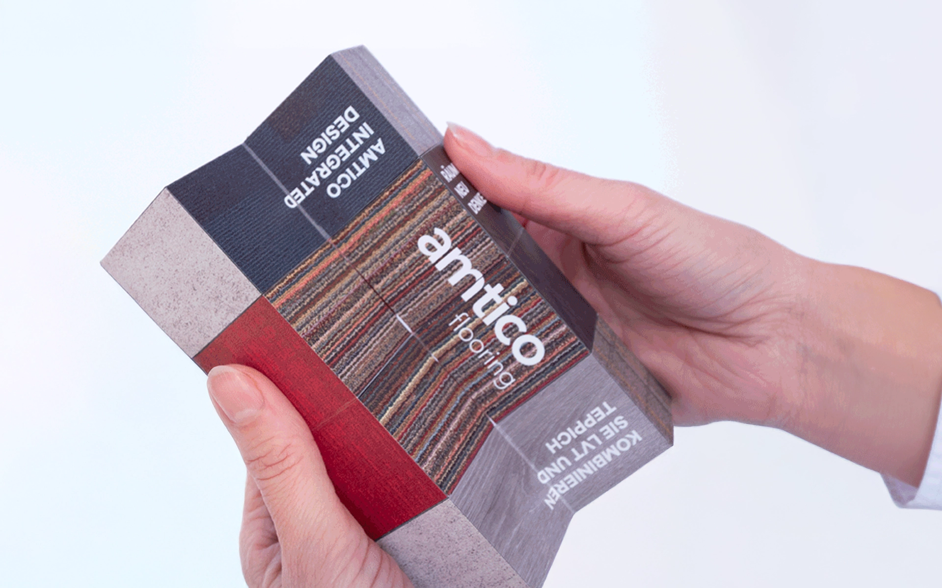 B2B mailing for Amtico flooring with an unfolded cube, held by two hands, with material samples of carpet and vinyl