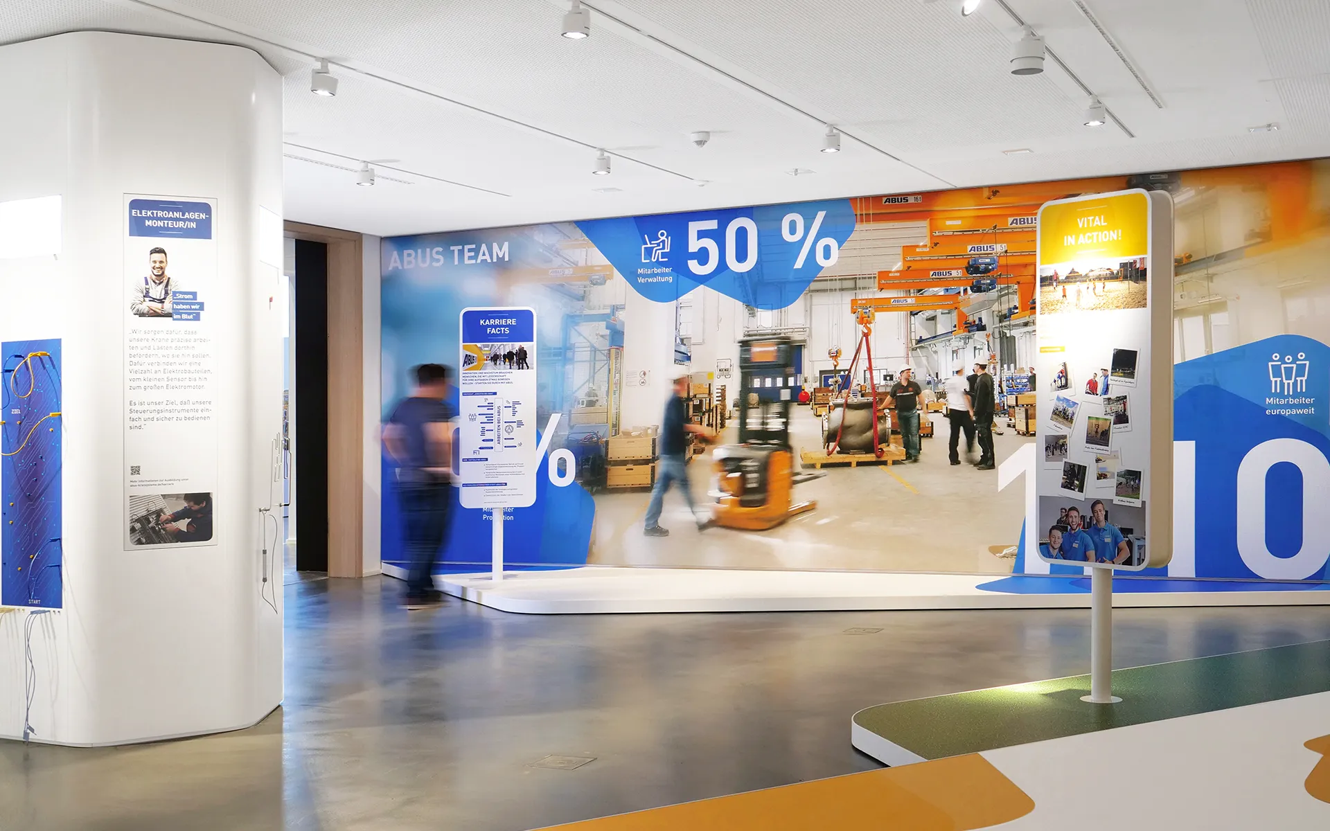 Interaktive Ausstellung und Kommunikationskonzept eines Showrooms für ABUS Kransysteme mit großflächigen Infowänden, Leuchtgrafiken und Besucher:innen in Bewegung