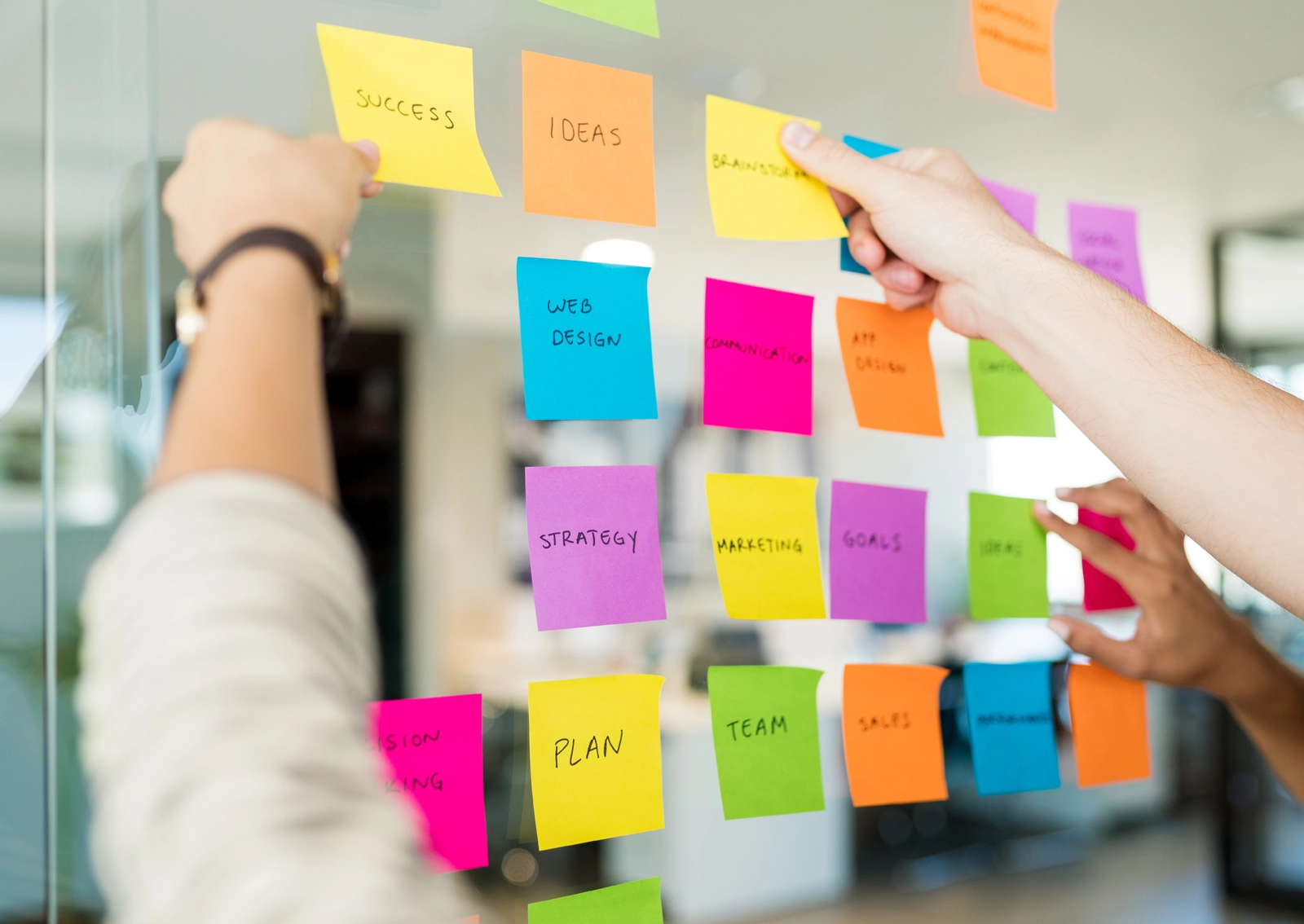 Shot from an R211 workshop for developing a user journey: Two people stick Post-its on a glass wall and sort thematically relevant content.