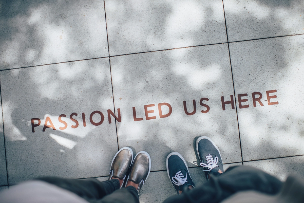 Image of a floor statement with the inscription 'Passion led us here'. Two people stand in front of it, only their feet are visible – as a symbol for the starting point of a shared brand journey. Context: Branding.