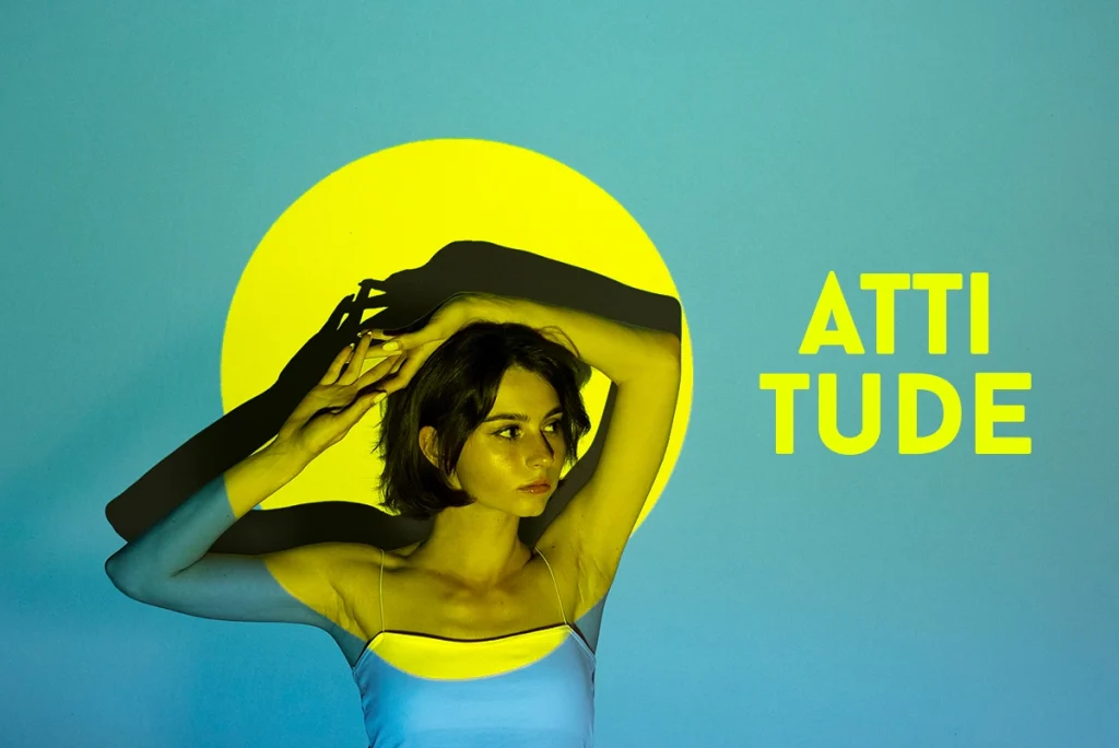 A woman crosses her arms over her head, behind her is the word "Atitude"