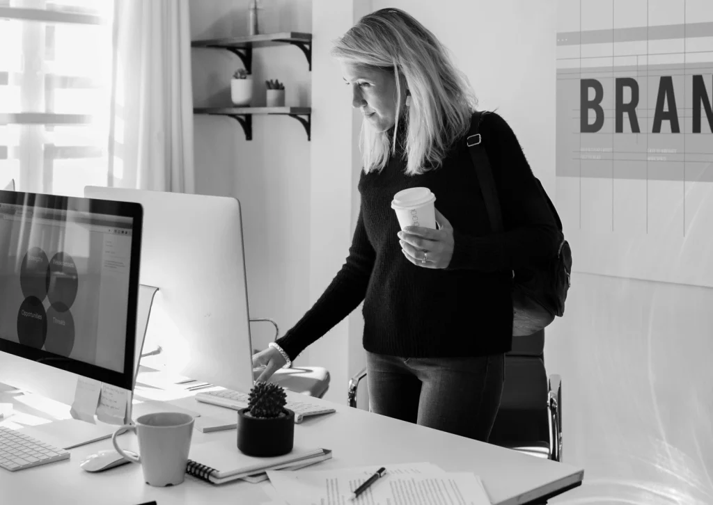A woman stands with a coffee mug at a desk in a design office